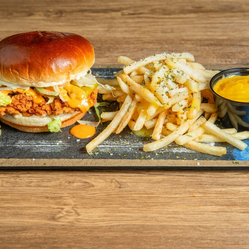 Crispy chicken burger with lettuce and sauce served alongside seasoned fries and cheese dipping sauce on a black platter.
