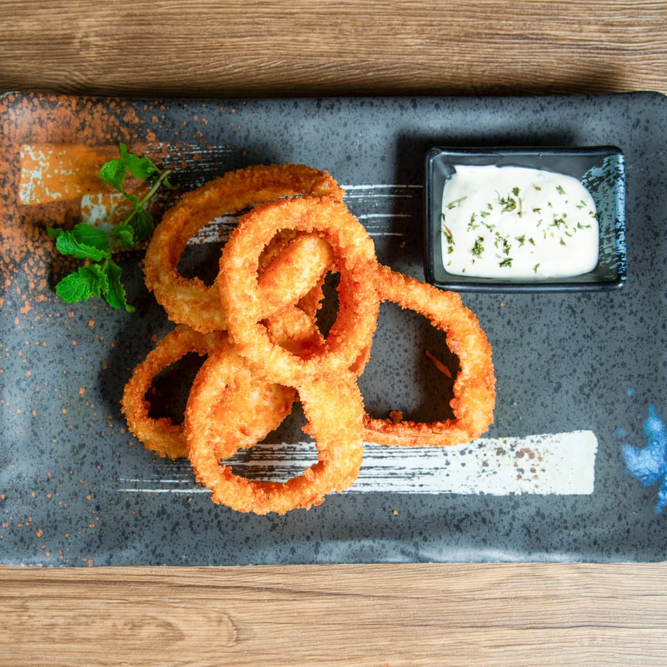 Crispy golden onion rings served on a rustic dark plate with herb-garnished dipping sauce and mint garnish.