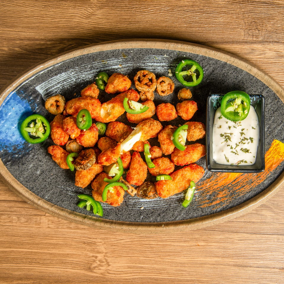 Crispy orange chicken pieces topped with sliced jalapeños, served with herb ranch dipping sauce on a decorative platter.