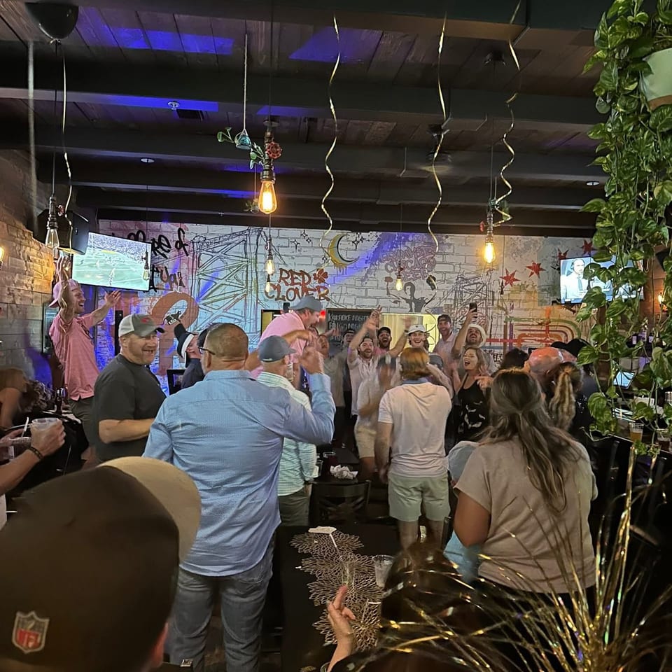 Crowded restaurant guests celebrate beneath string lights and blue accents, surrounded by graffiti-style murals, televisions, and festive decorations.