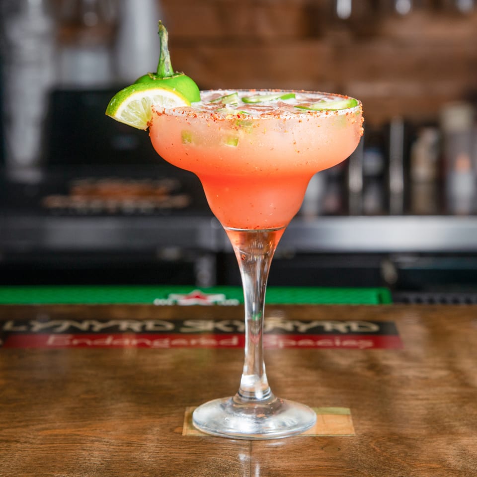 Bright pink margarita in a salt-rimmed glass garnished with lime, displayed on a restaurant bar.