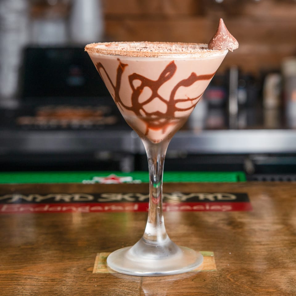 Chocolate-drizzled creamy cocktail in a sugar-rimmed martini glass, topped with a chocolate swirl, on a bar counter.