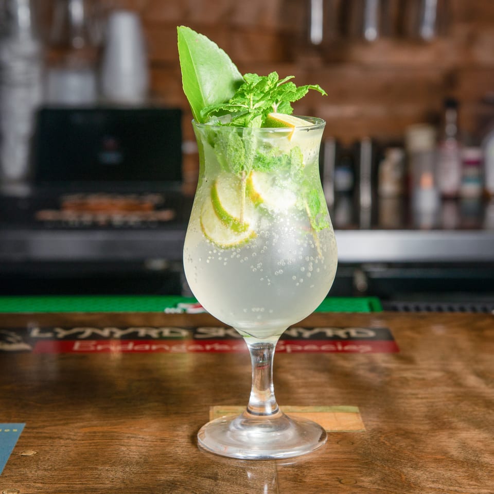 Sparkling lime and mint cocktail served in a stemmed glass on a wooden bar counter.