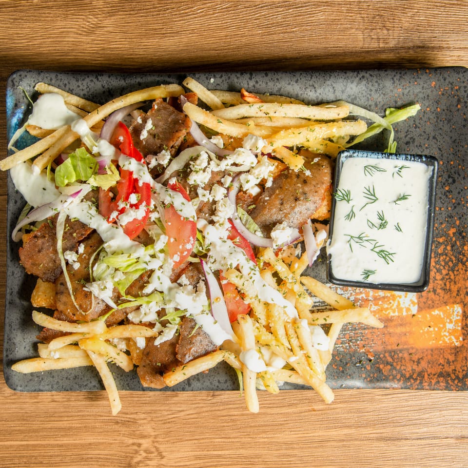 Greek-style platter with grilled meat, fries, lettuce, tomatoes, onions, feta, and dill-topped tzatziki sauce.